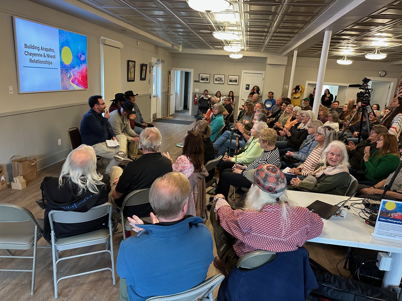 Packed community gathering at a presentation titled 'Building Arapaho, Cheyenne & Niwot Relationships' in Niwot, Colorado